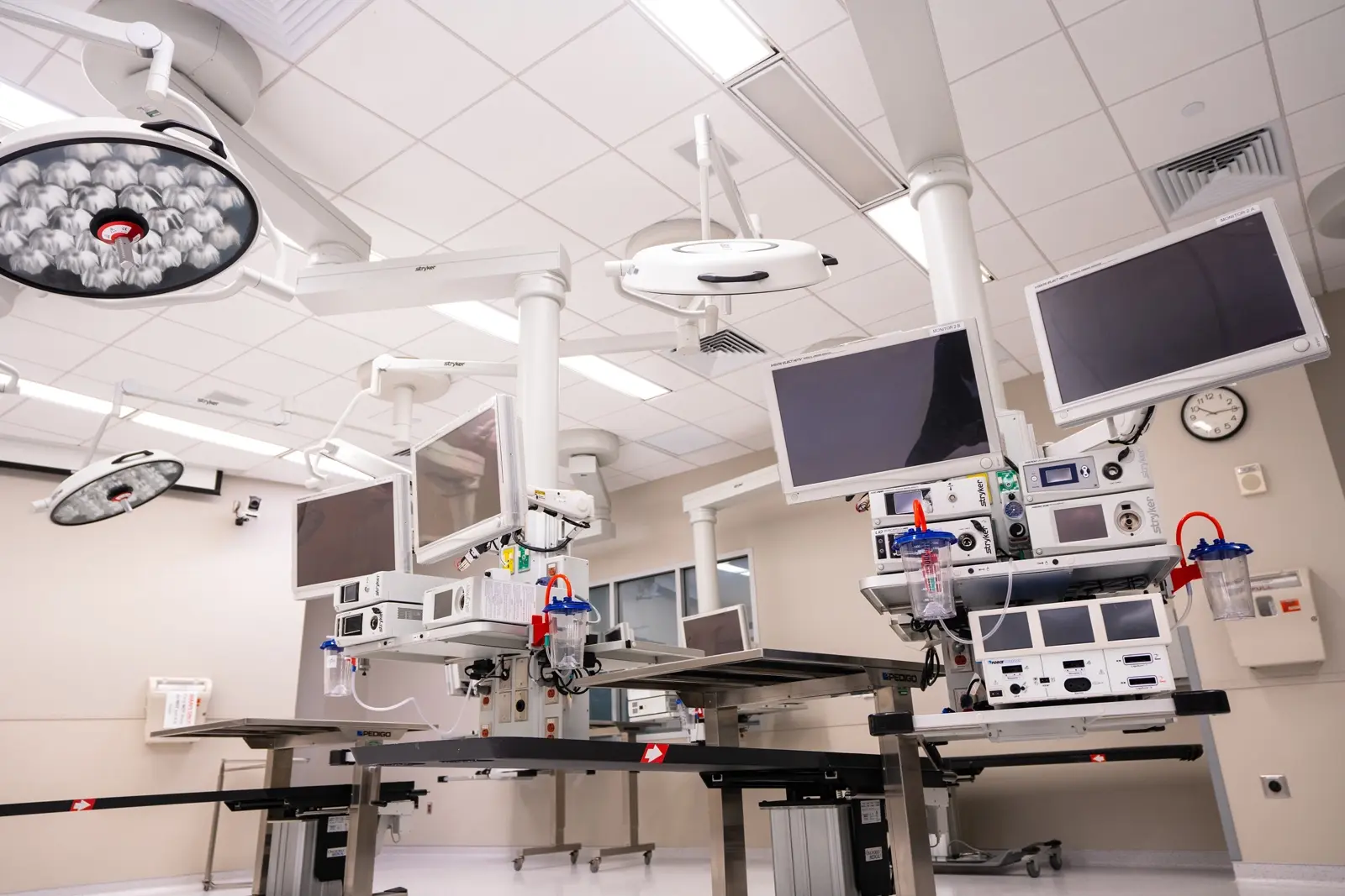 CAMLS A modern, sterile hospital operating room with multiple monitors, surgical lights, and advanced medical equipment. The room is well-lit with white walls and ceiling, and there are empty operating tables in the center.